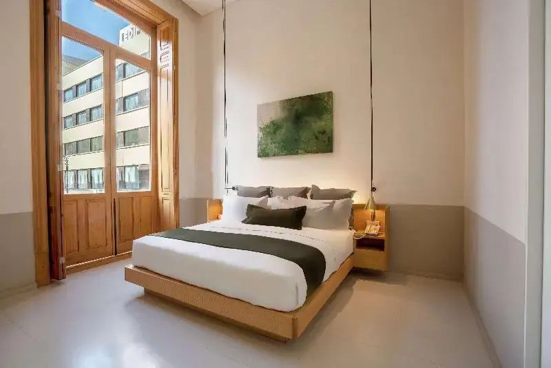 Doppelbett mit weißer Bettwäsche, grüner Tagesdecke und Blick auf das Nachbargebäude.