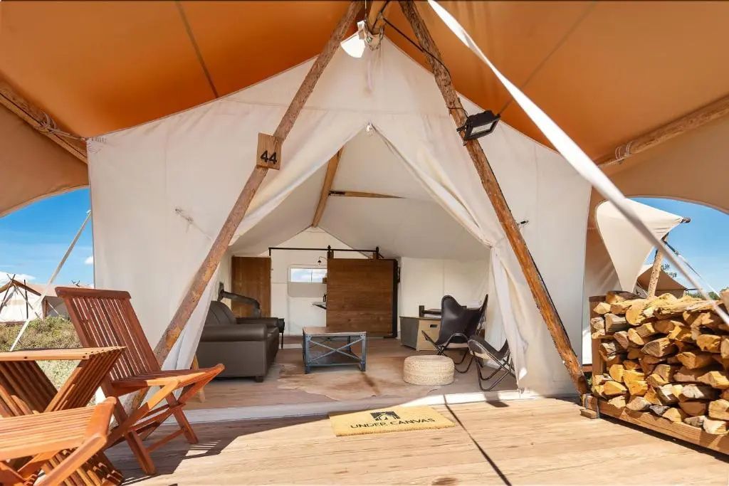 Überdachte Holzterrasse mit Stühlen am Eingang eines Glampingzeltes.