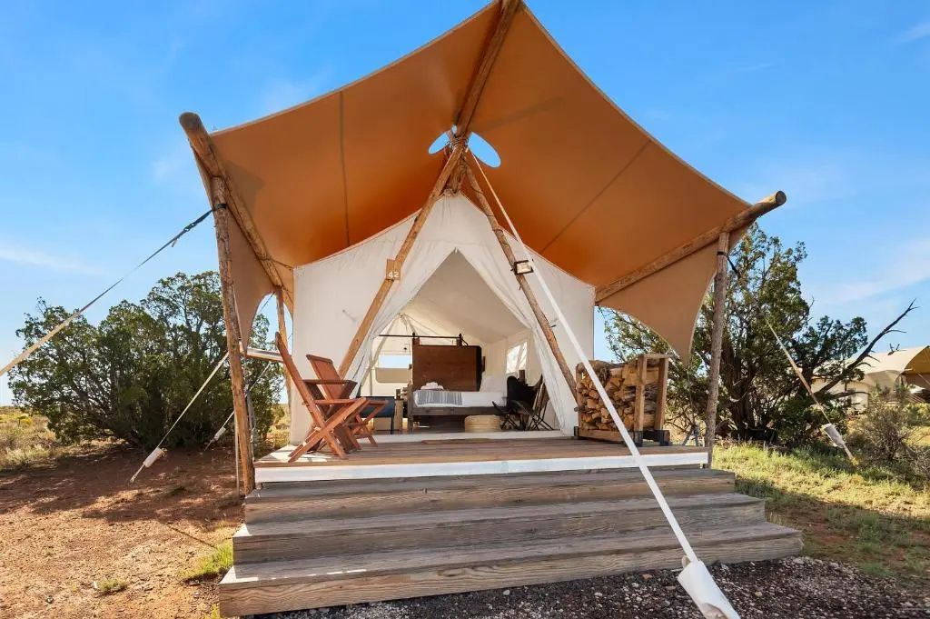Ein aufgebautes Safari-Zelt mit Holzterrasse und Stufen inmitten von Natur.