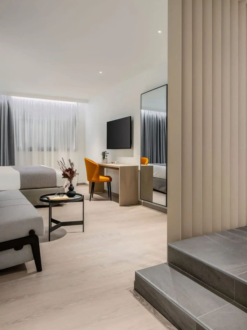 Modernes Hotelzimmer mit Schreibtisch, orangefarbenem Stuhl, Fernseher und Wandspiegel.