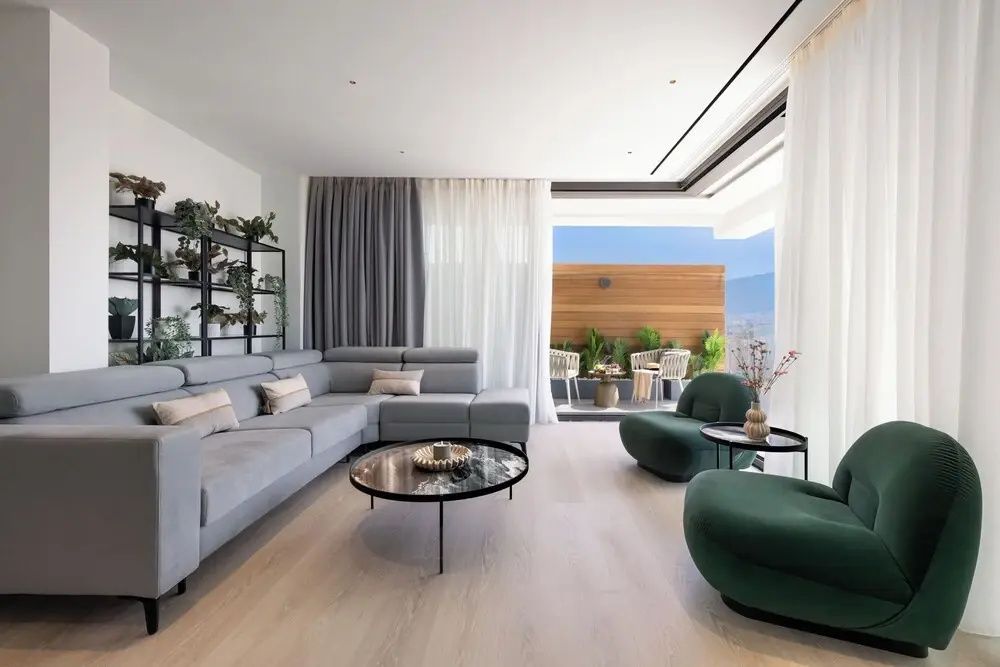 Helles Wohnzimmer mit grauer Eckcouch, grünen Sesseln und Zugang zur überdachten Terrasse.