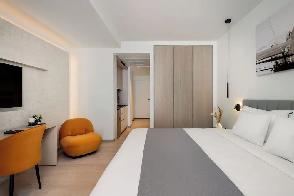 Blick in ein modernes Hotelzimmer mit gelbem Sessel, holzfarbenem Kleiderschrank und Flurbereich.