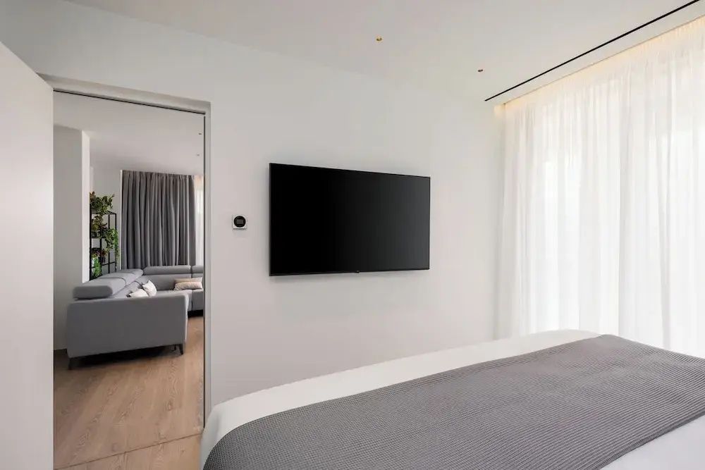Wandmontierter Flachbildfernseher im Schlafzimmer mit Blick auf den angrenzenden Wohnbereich.