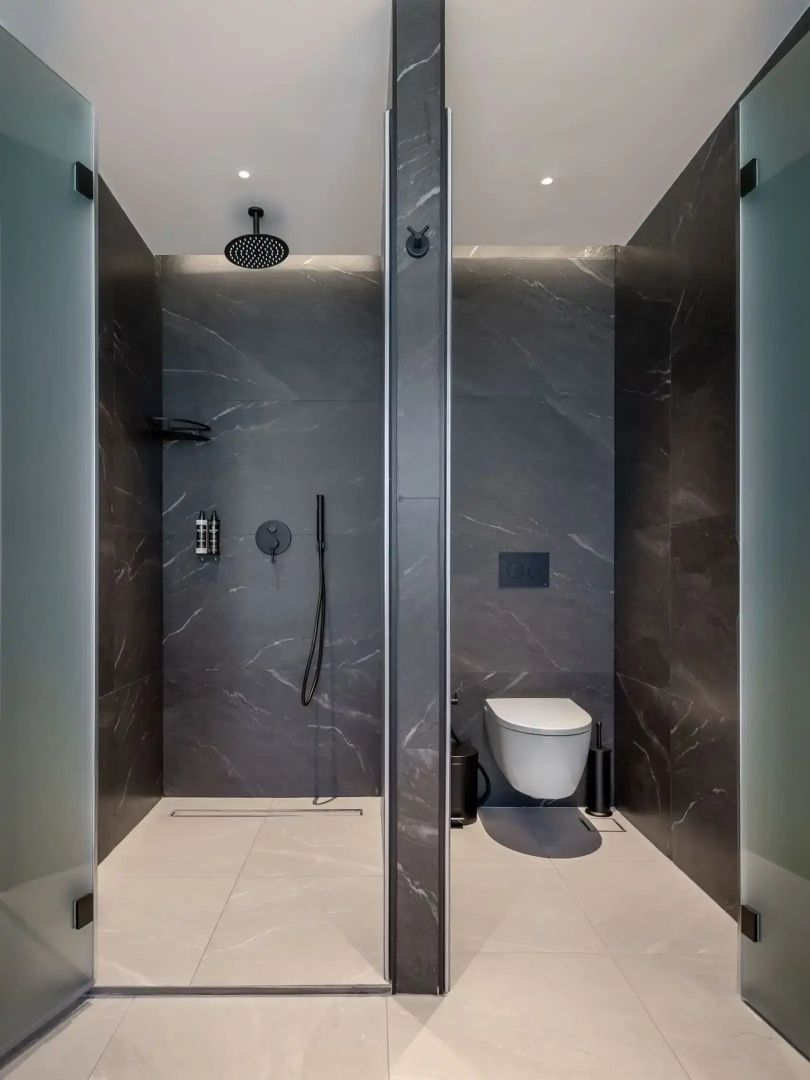 Badezimmer mit dunklen Marmorwänden sowie einer ebenerdigen Regendusche und WC.