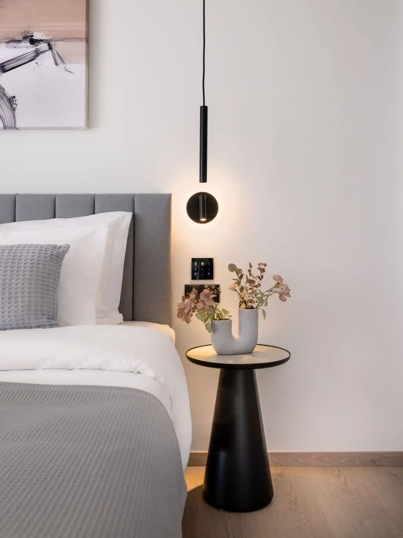 Ein Nachttisch mit Blumen in einer Vase und eine schwarze Hängeleuchte neben dem Bett.