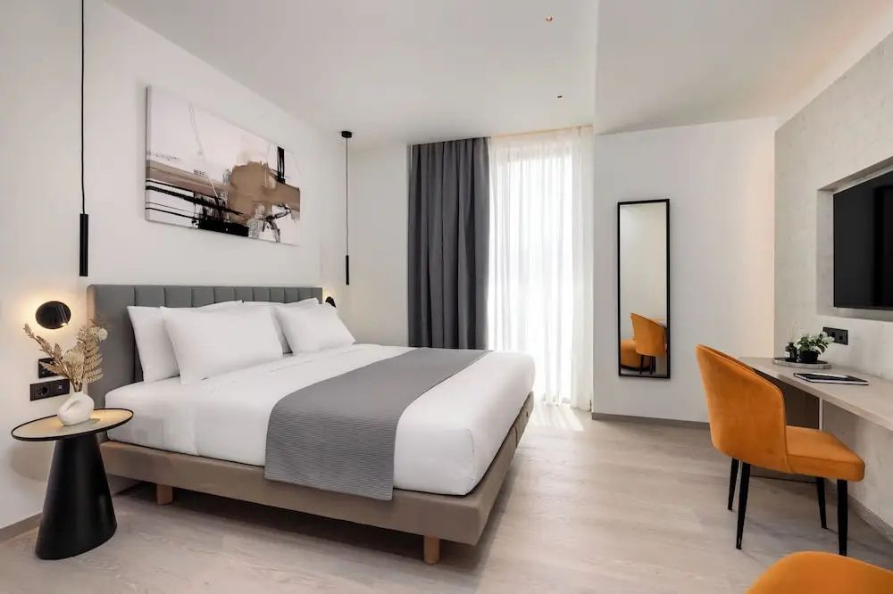 Helles Doppelzimmer mit weißer Bettwäsche, grauer Tagesdecke und modernem Wandbild.