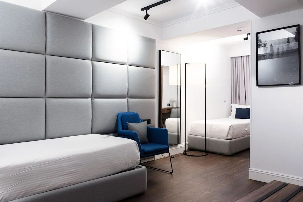Modernes Hotelzimmer mit zwei Einzelbetten, blauem Sessel und dunklem Holzboden.