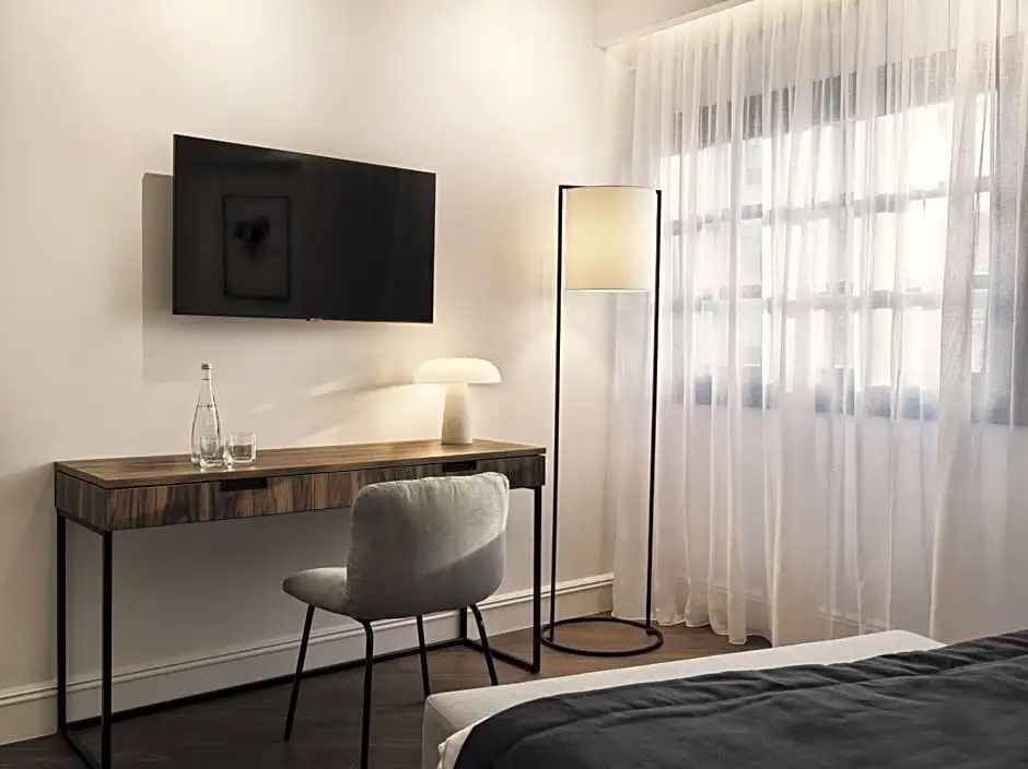 Schreibtisch mit Stuhl, Wand-Fernseher und Stehleuchte im hellen Hotelzimmer.
