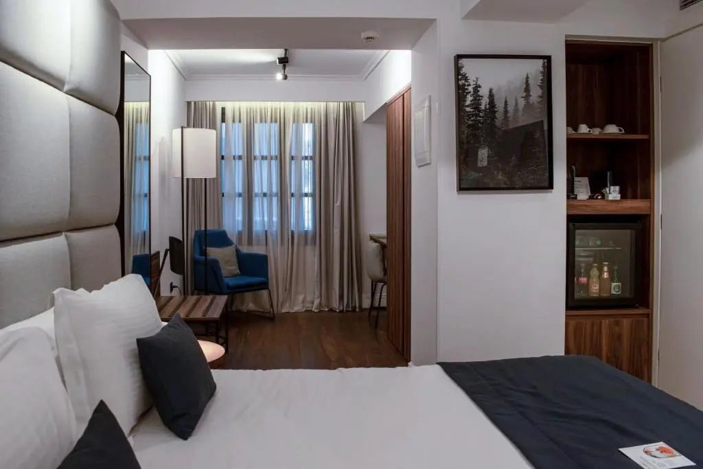 Blick durch das Hotelzimmer auf einen blauen Sessel und ein Fenster mit Vorhängen.