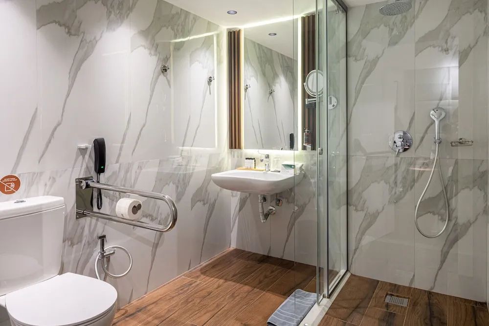 Barrierefreies Badezimmer mit Dusche, Haltegriff am WC und Holzoptik-Boden.