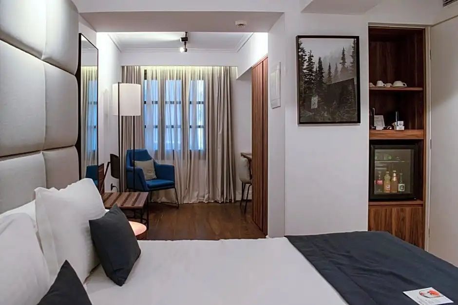 Blick in ein modernes Hotelzimmer mit Doppelbett, blauem Sessel und hellen Vorhängen am Fenster.