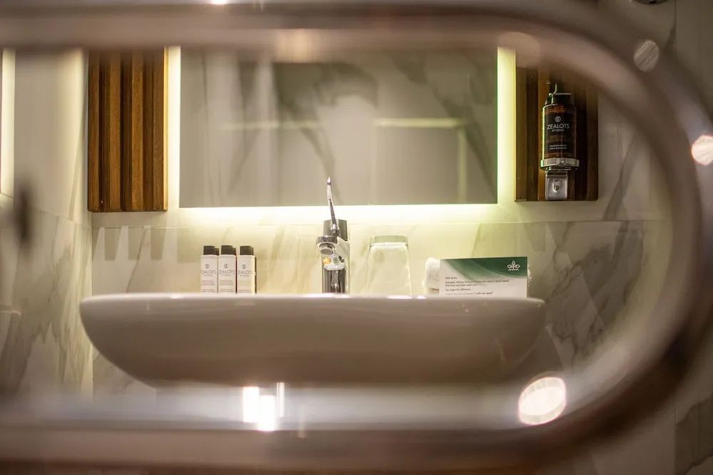 Waschbecken im Badezimmer mit Wasserhahn, Spiegel und kleinen Pflegeprodukten.