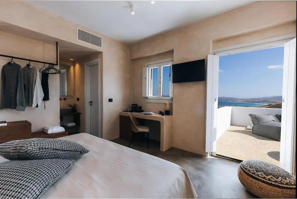 Hotelzimmer mit Doppelbett, Schreibtisch, Fernseher und geöffneter Tür zur Terrasse mit Meerblick.