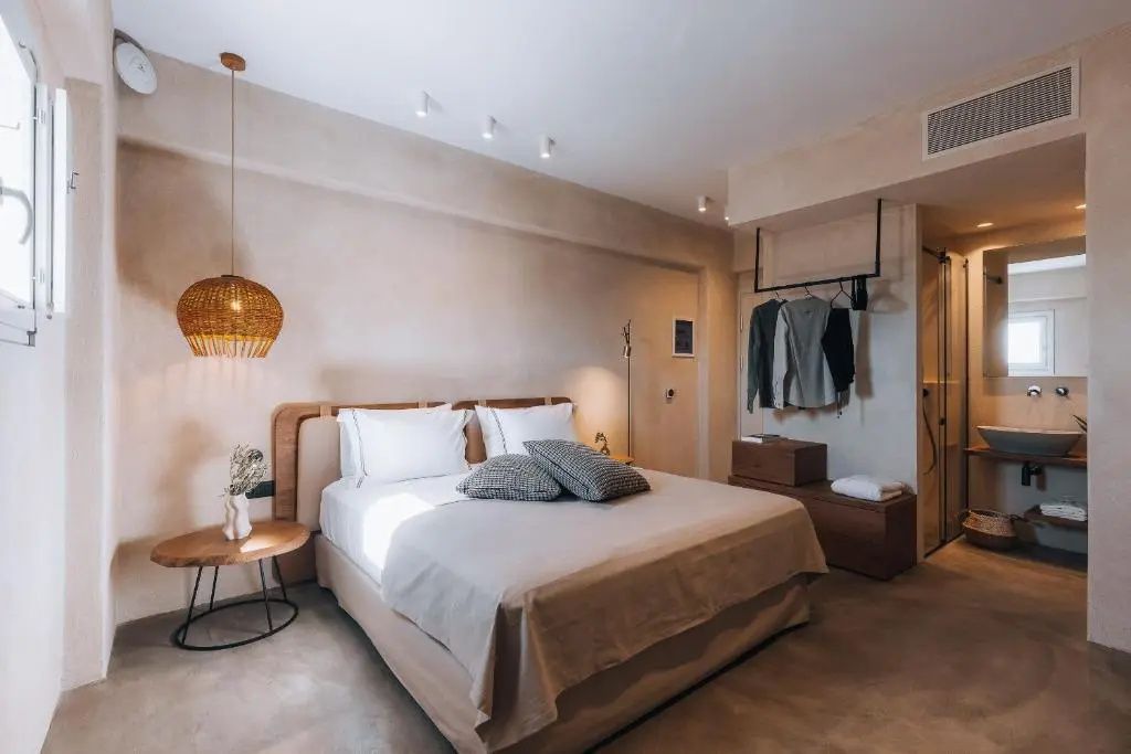 Doppelbett im Hotelzimmer mit hellen Kissen, Nachttisch aus Holz und geflochtener Hängelampe an der Wand.