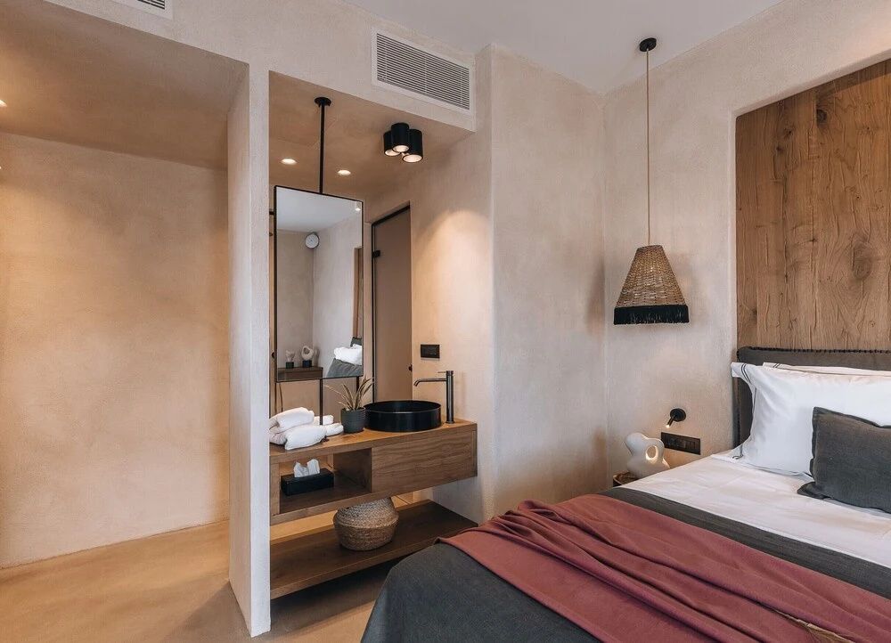 Modernes Hotelzimmer mit hellen Wänden, einem Doppelbett und offenem Waschtischbereich mit Holzkonsole.