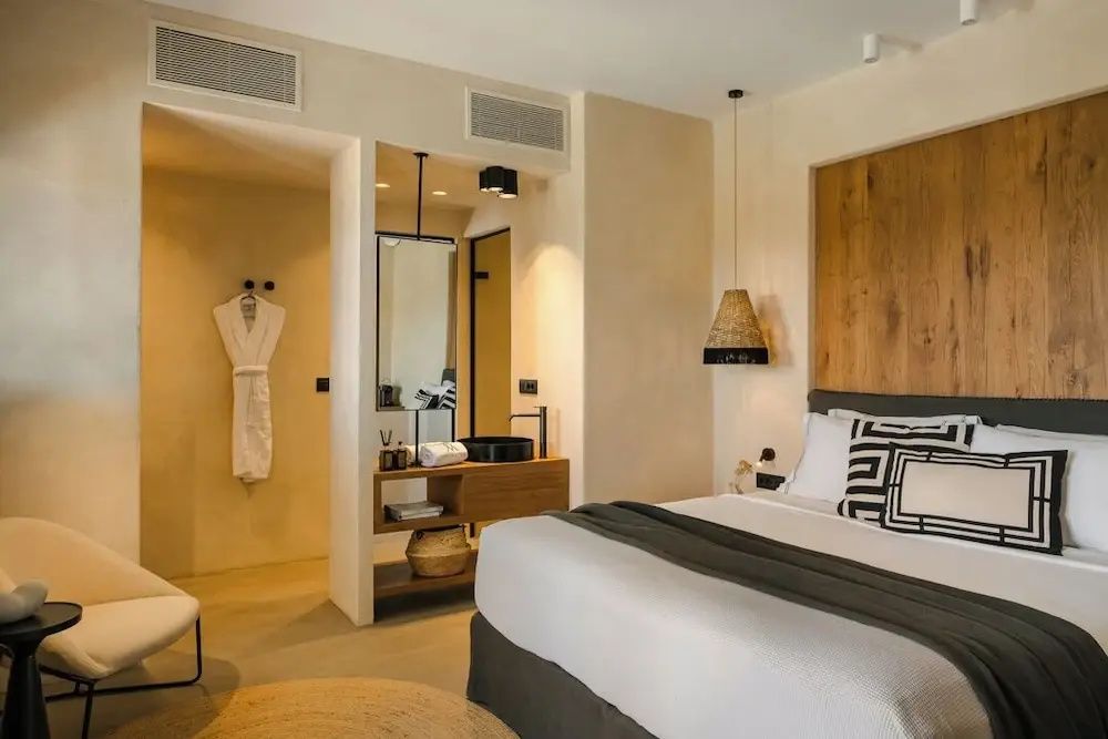 Hell eingerichtetes Hotelzimmer mit Doppelbett, Hängeleuchte, Bademantel und integriertem Waschbereich.