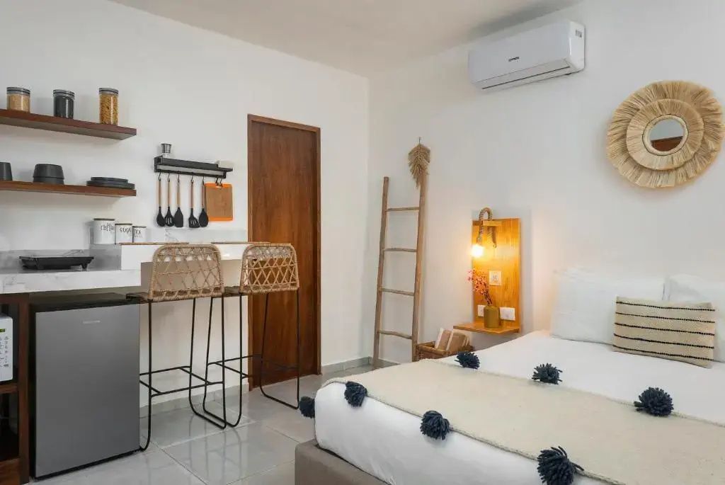 Helles Studio-Zimmer mit Bett, kleiner Küchenzeile mit Barhockern und Holzdeko.