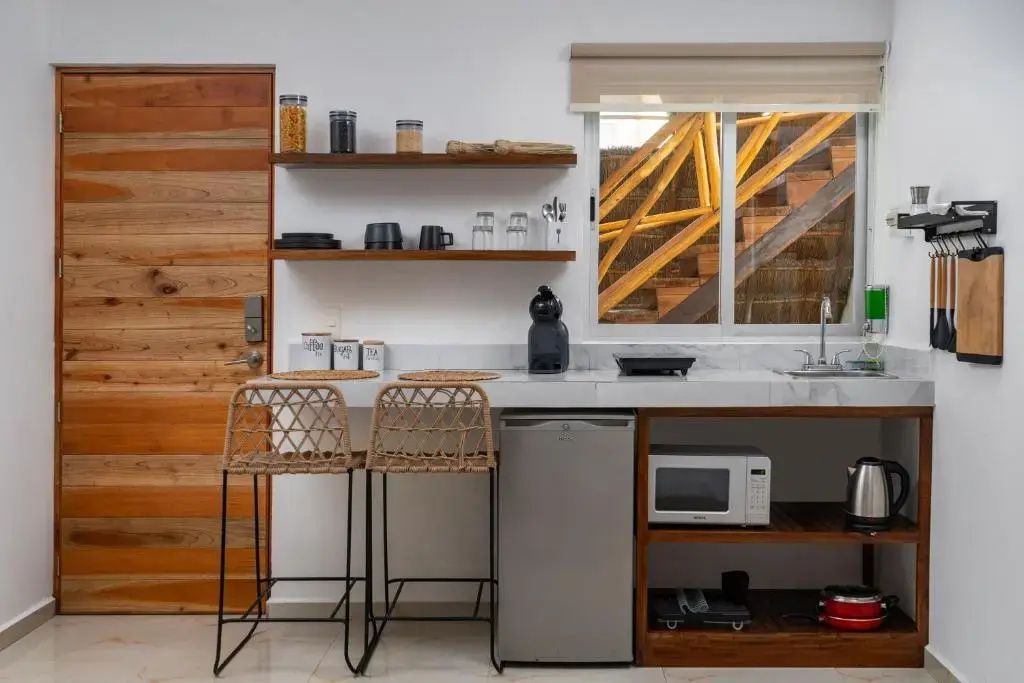 Kleine Küchenzeile in einem Studio mit zwei Barstühlen an der Theke, Kühlschrank und Regalen.