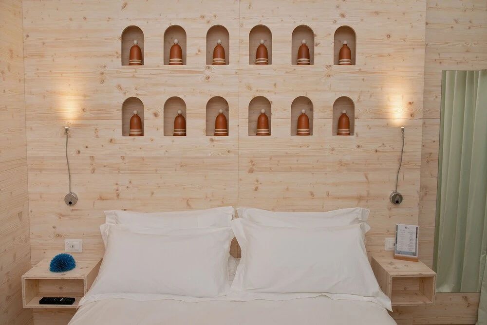 Bett mit weißen Kissen vor einer hellen Holzwand mit kleinen Wandnischen.