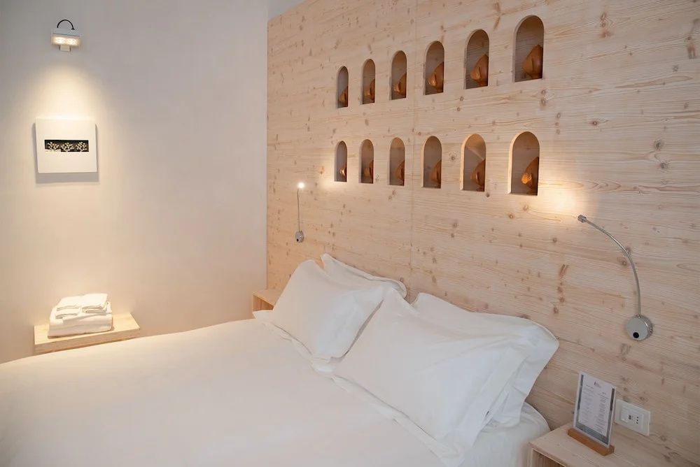 Ein weiß bezogenes Doppelbett vor einer Holzwand mit kleinen beleuchteten Nischen.