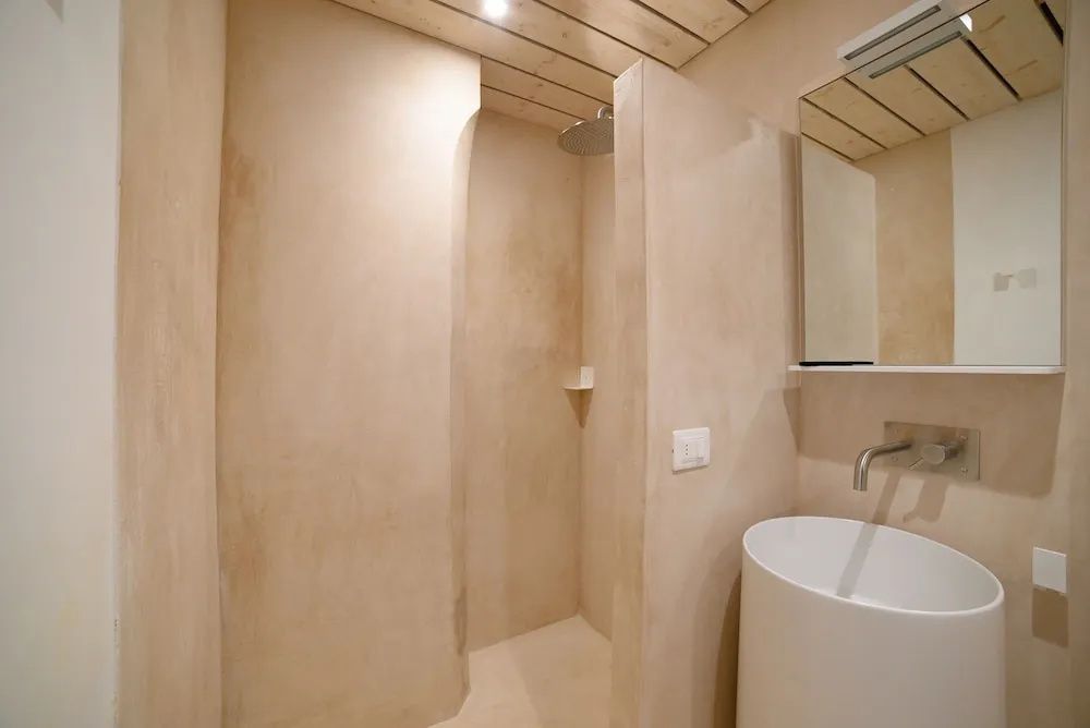 Badezimmer mit verputzten Wänden, begehbarer Dusche und rundem Waschbecken.