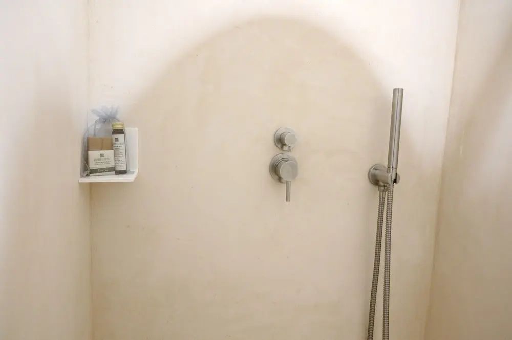Moderne Dusche mit beigefarbener Wand, silberner Armatur und Handbrause.