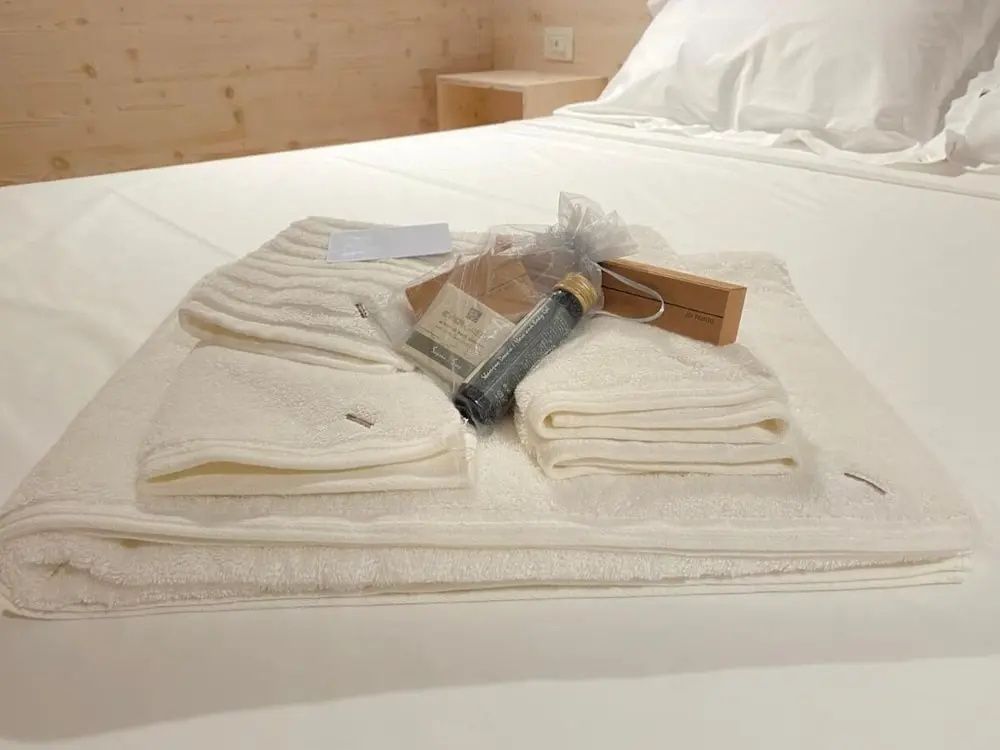 Zusammengelegte weiße Handtücher und Pflegeprodukte auf einem hellen Bett.