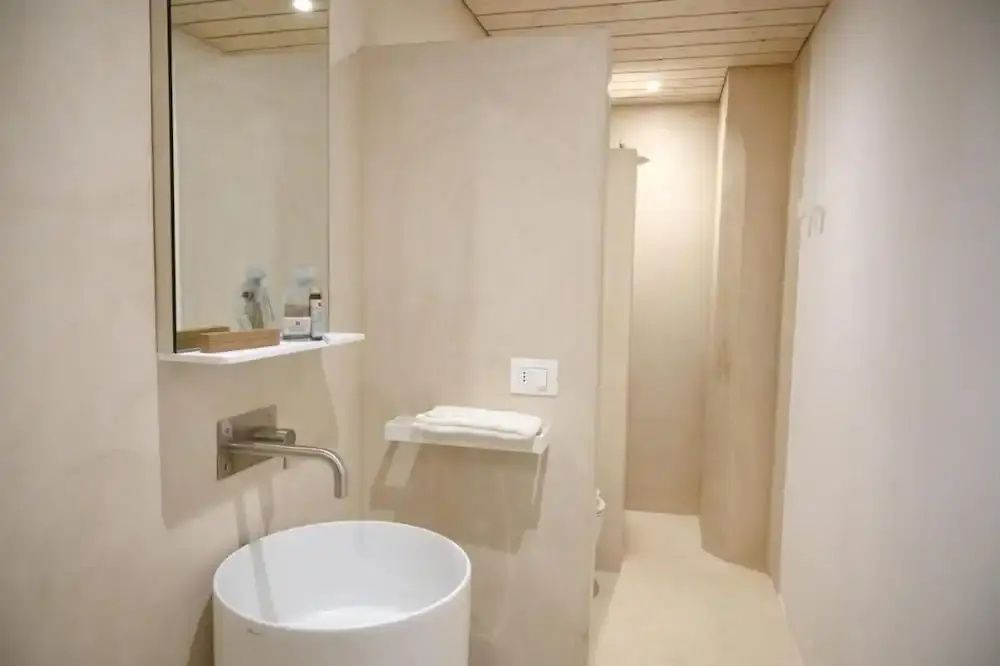Modernes Badezimmer in beigen Tönen mit einem runden Aufsatzwaschbecken und Spiegel.