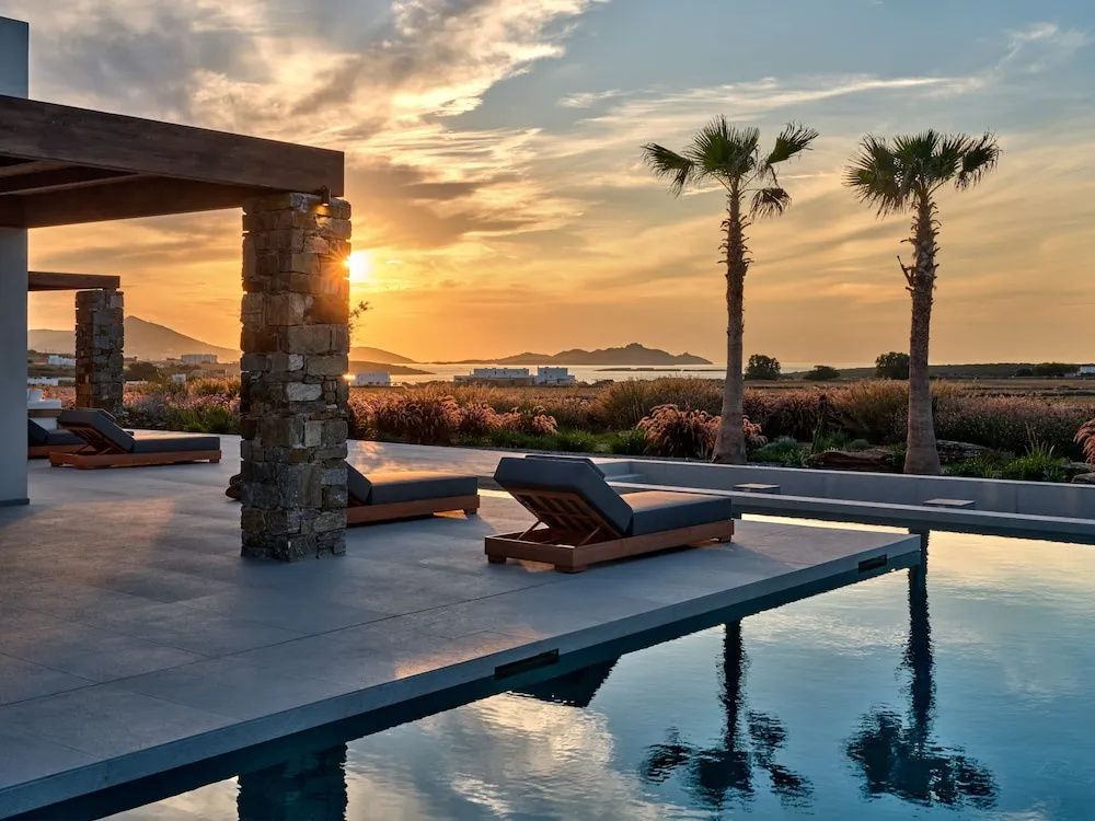 Terrasse mit Swimmingpool, Sonnenliegen und Blick auf das Meer bei Sonnenuntergang.