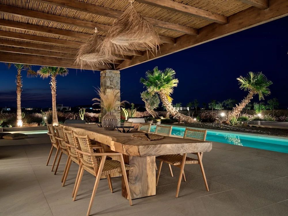 Überdachte Terrasse mit großem Holztisch und Beleuchtung neben dem Pool.