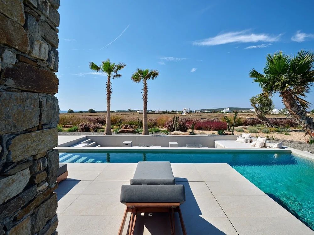 Terrasse mit Sonnenliege und Swimmingpool mit Blick auf Palmen und die umliegende Landschaft.
