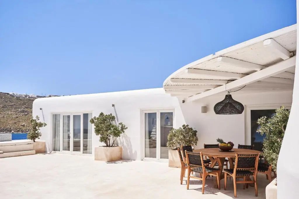 Weiß gestalteter Außenbereich der Villa mit Holztisch und schattspendender Überdachung.