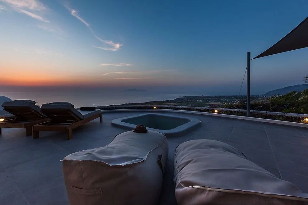Terrasse mit einem Whirlpool und Sitzkissen bei Blick auf das Meer in der Dämmerung.
