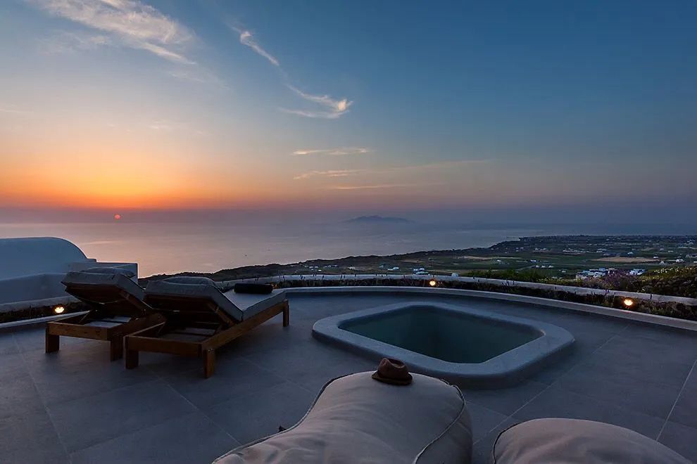 Terrasse mit Whirlpool und Liegen während des Sonnenuntergangs über dem Meer.
