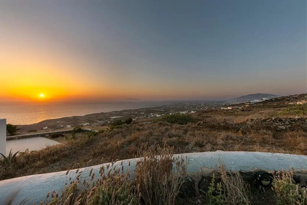 Weite Küstenlandschaft mit trockenem Bewuchs und Blick auf das Meer bei Sonnenuntergang.