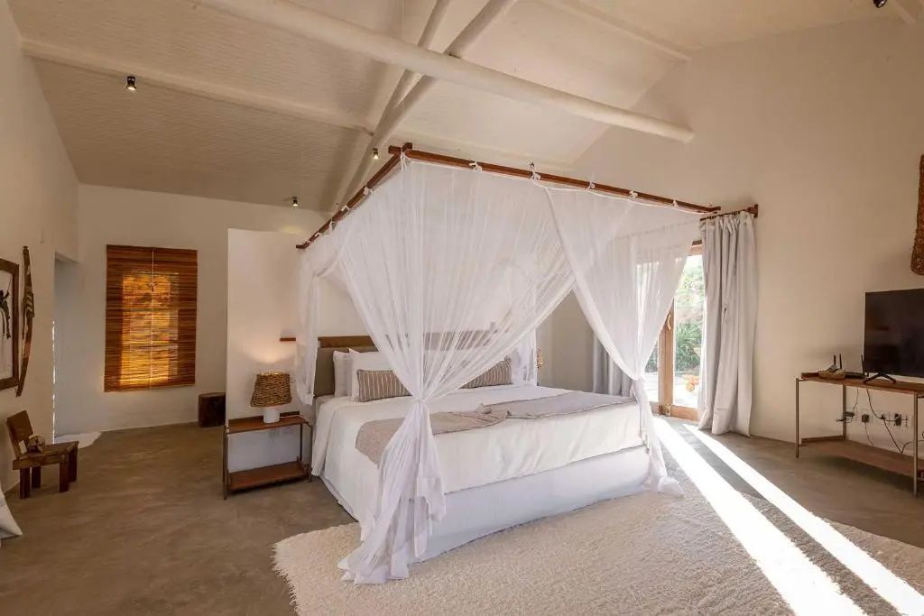 Schlafzimmer mit einem großen Doppelbett, weißem Moskitonetz und hellem Teppich.