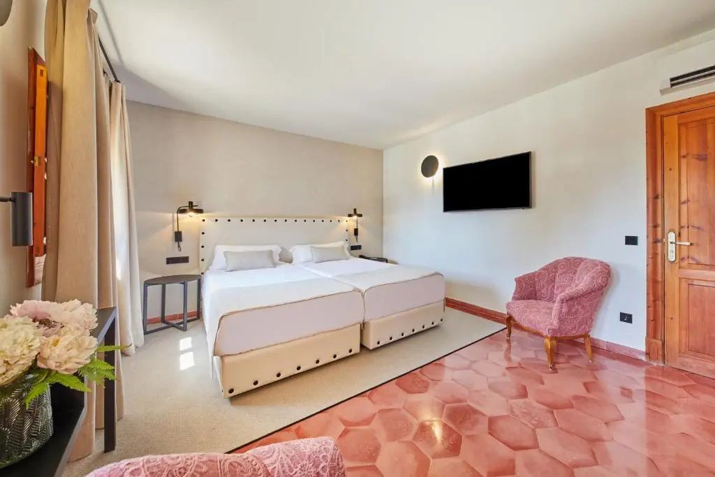 Schlafzimmer mit Doppelbett, Wandfernseher, rosa Sessel und rotem Fliesenboden.