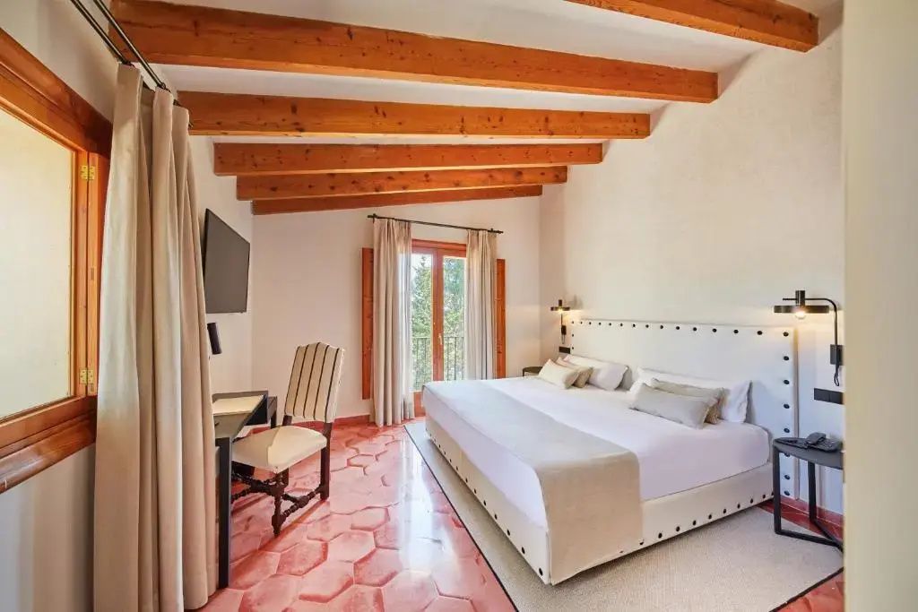 Helles Schlafzimmer mit Doppelbett, Schreibtisch, Wandfernseher und Fliesenboden.
