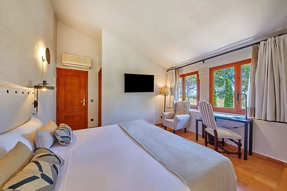 Einrichtetes Hotelzimmer mit Bett, Fernseher, Sessel und Fenstern ins Grüne.