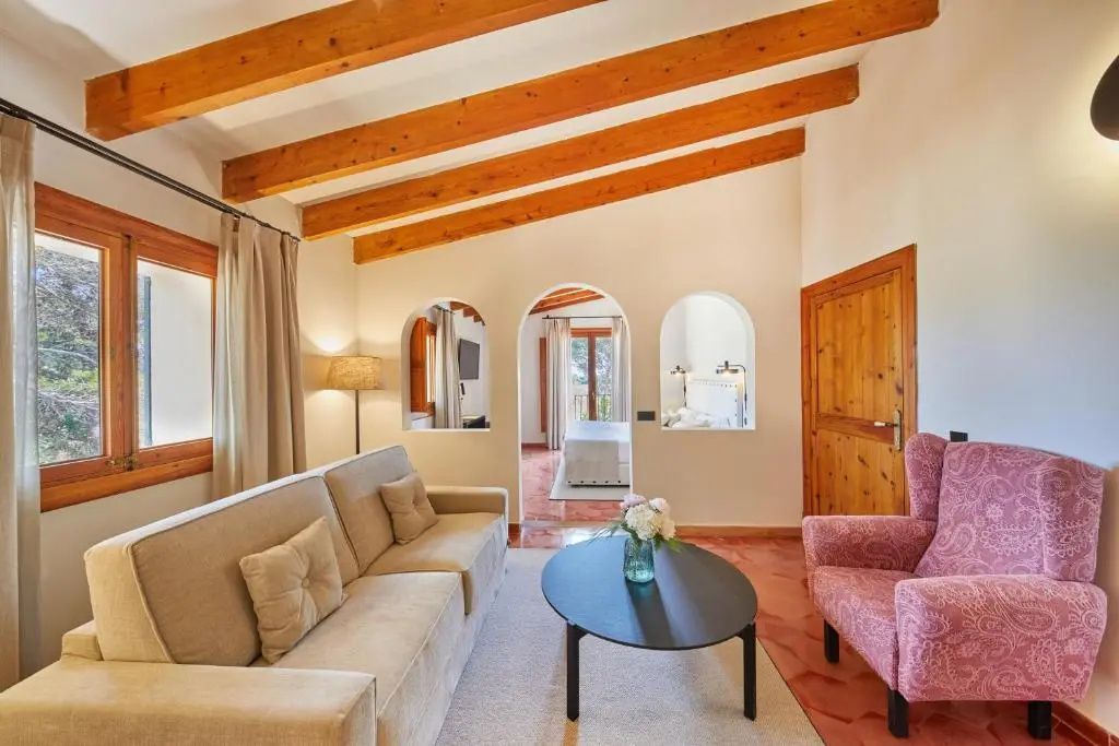 Wohnbereich mit beigefarbenem Sofa, rosa Sessel und Holzdeckenbalken im Finca-Stil.