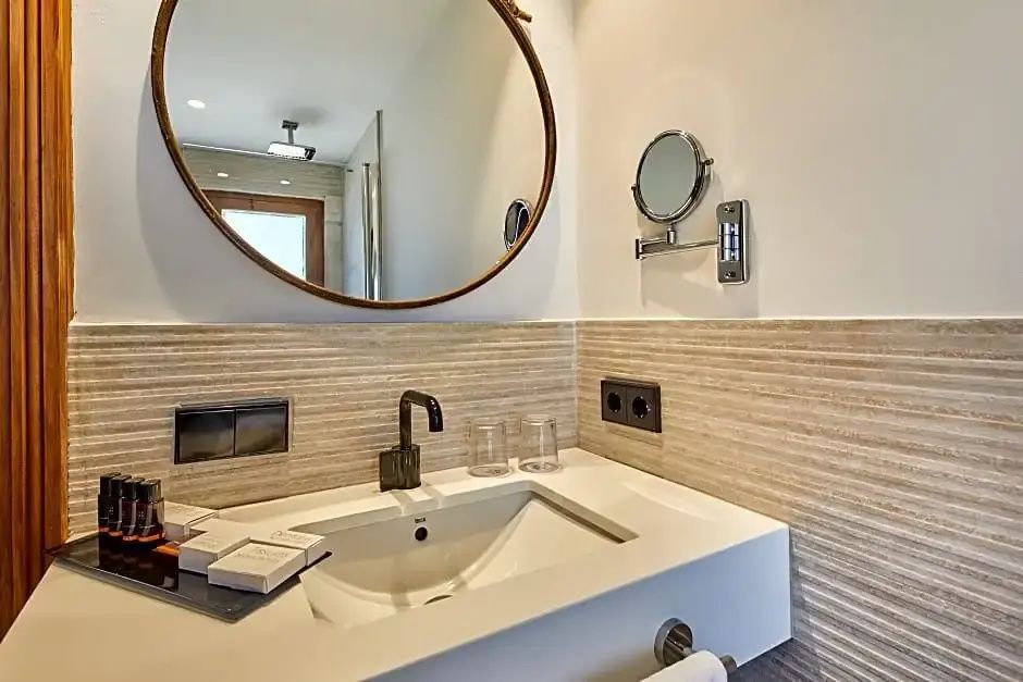 Waschbecken mit dunkler Armatur, rundem Spiegel und Pflegeprodukten im Badezimmer.