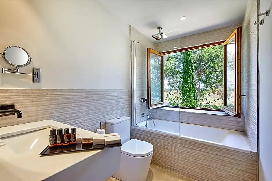Badezimmer mit Badewanne, Glasduschwand, Toilette und geöffnetem Holzfenster.