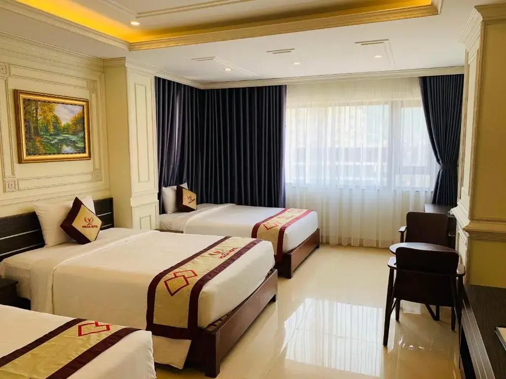 Geräumiges Hotelzimmer mit mehreren Betten, hellen Vorhängen und Holzstühlen.