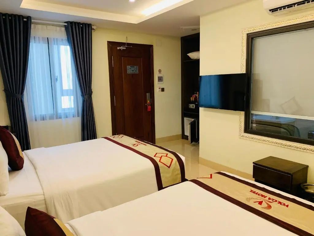 Hotelzimmer mit zwei Doppelbetten, Fernseher an der Wand und Holztür.