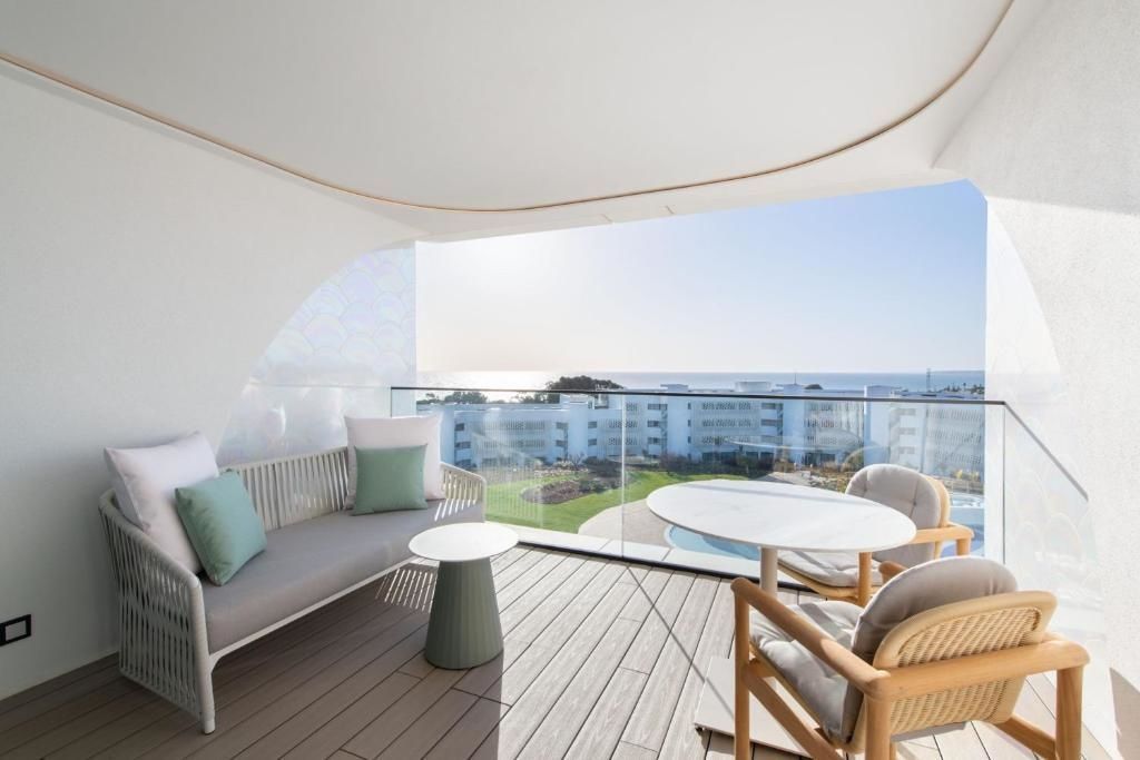 Überdachter Balkon mit modernen Sitzmöbeln, Holzboden und Blick über die Anlage auf das Meer.