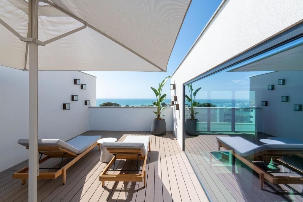 Dachterrasse mit zwei Sonnenliegen unter einem Sonnenschirm und Meerblick.