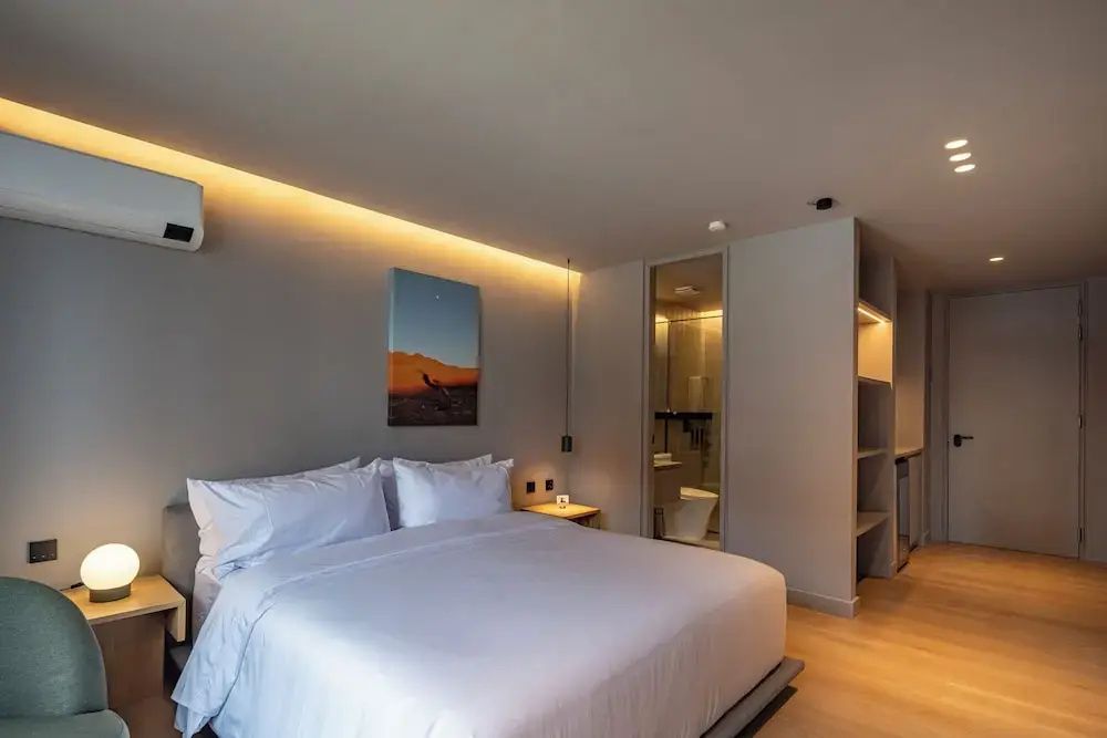 Doppelbett mit weißer Bettwäsche, Wandbild, indirekter Beleuchtung und Glasbad.