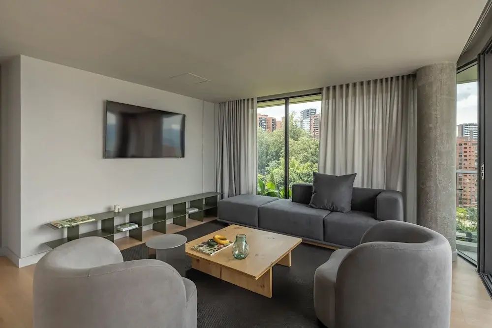 Modernes Wohnzimmer mit grauer Couch, Holzcouchtisch und Blick durch ein großes Fenster.