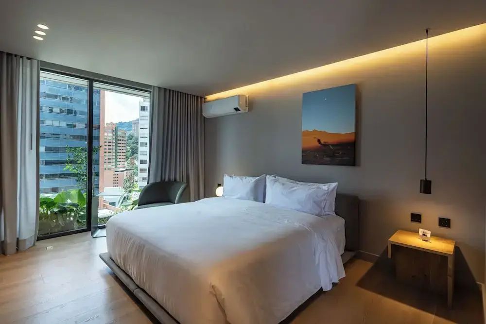 Schlafbereich mit großem Doppelbett, Sessel und bodentiefem Fenster mit Stadtblick.
