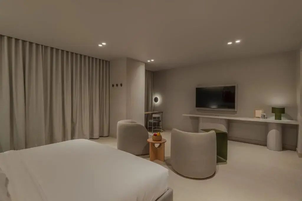 Wohnbereich des Hotelzimmers mit Fernseher, zwei Sesseln und Schreibtisch.